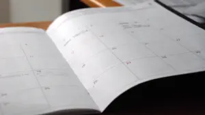 Atvērts mēneša plānotājs uz koka galda virsmas mierīgai plānošanai.