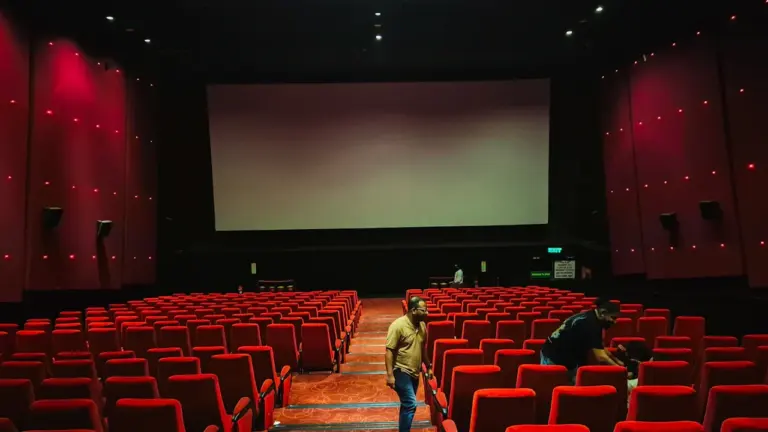 Tukša kinoteātra zāle ar sarkanām sēdvietām un lielu ekrānu pirms filmu seansa.