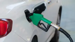 Degvielas uzpildes pistole ievietota baltas automašīnas bākā degvielas uzpildes stacijā.