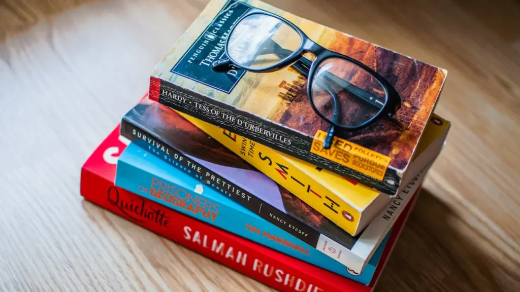Lasīšanas brilles uz krāsainu grāmatu kaudzes, simbolizējot valodu apguvi un literatūru.