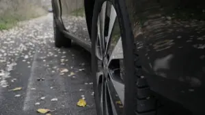 Automašīnas riepa uz ceļa, kas klāts ar rudens lapām, gatavošanās braukšanai rudenī.