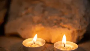 Divas degošas tējas sveces uz smilšainas virsmas ar akmeni fonā siltā apgaismojumā.