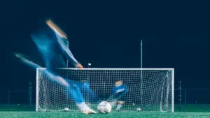 Futbola treniņš vakarā, spēlētājam izpildot sitienu pa vārtiem ar kustības efektu.