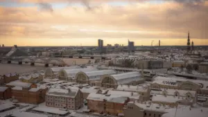 Panorāmas skats uz Rīgu ziemā ar sniegu klātiem pilsētas jumtiem.