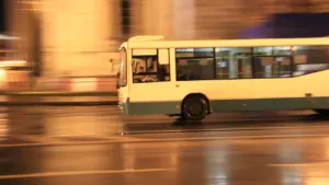 Balts autobuss ātri brauc pa pilsētas ielu vēlā vakara tumsā